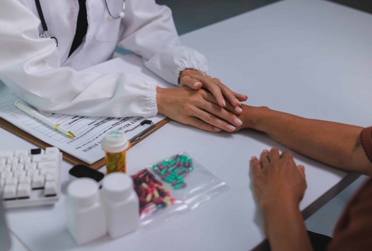 Doctor holding a patient's hand beside a registration form and various medications, reflecting individualised addiction treatment planning