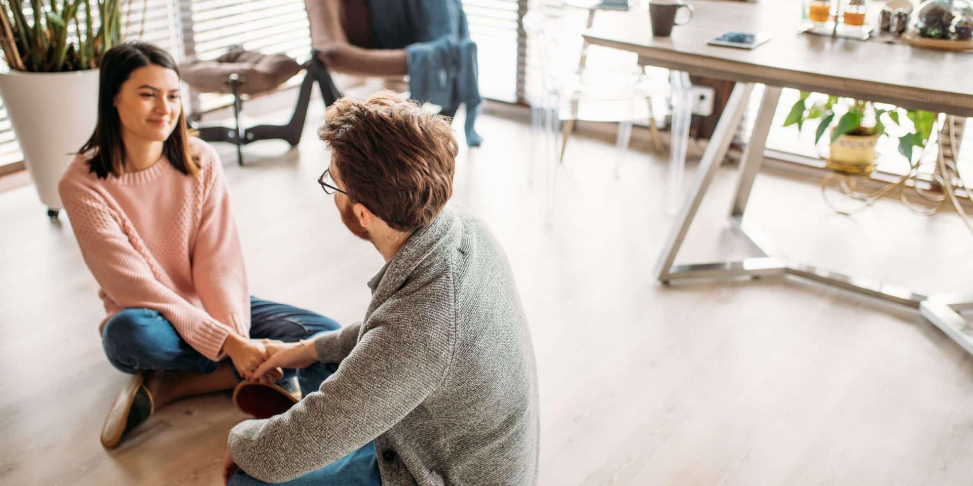 Man and woman sitting on the floor holding hands in conversation, representing supportive peer connection in recovery aftercare.