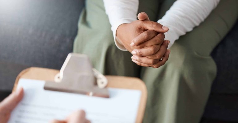 What Types of Therapies Are Offered at Rehabilitation Centres? 1 Client with clasped hands during a one-on-one counselling session, with a clinician's clipboard visible in the foreground